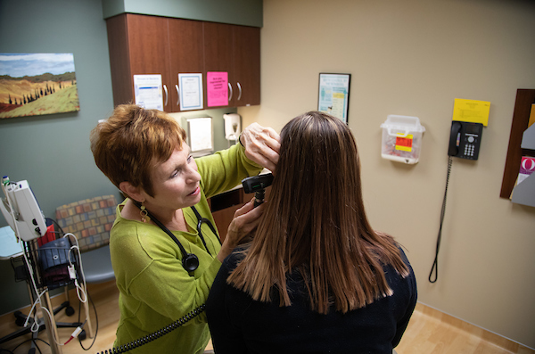 a doctor looks in the ear of a patient who is sitting on an exam table in the uno health center