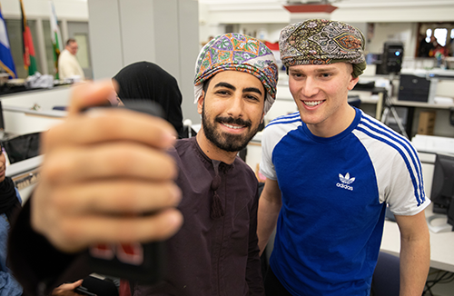 A student from Oman helps a student from the USA try on the traditional Omani men's headwear.