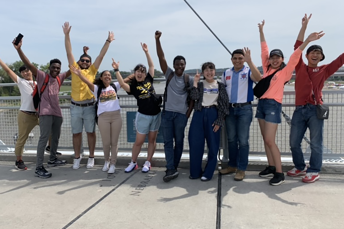 International students stand on the Bob Kerry Pedestrian Bridge, arms raised