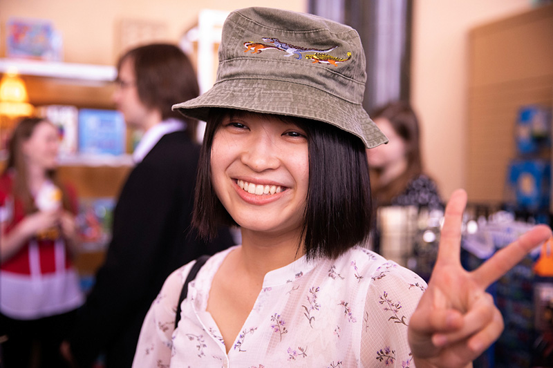 Japanese student tries on hat and shows peace sign with her hand.