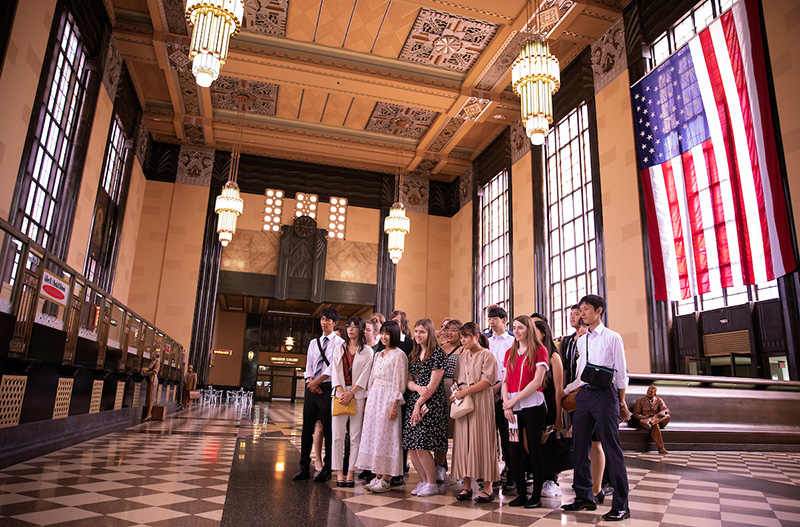 Japanese students tour Durham Museum and pose for group photo by American flag.