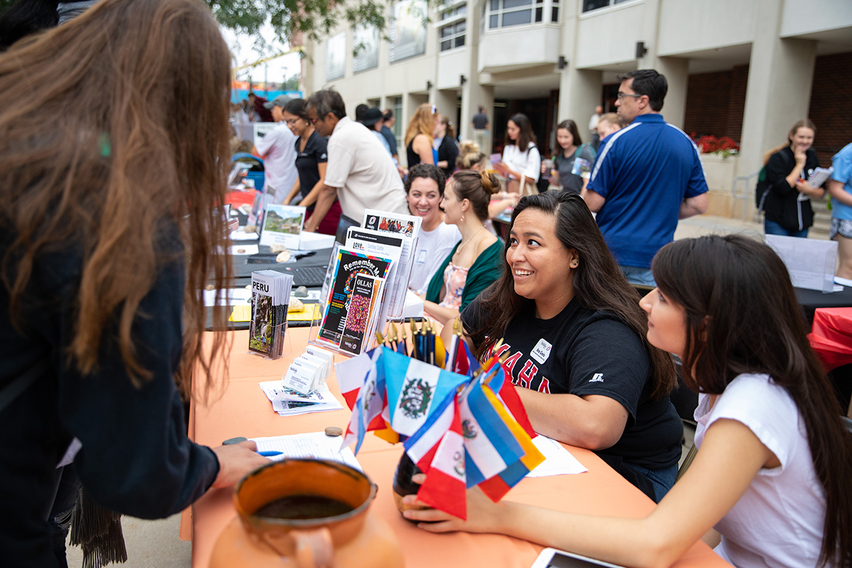 two women sit at a table at the study abroad fair, speaking with visitors to their table.