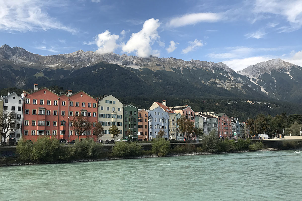A row of pastel colored houses along the waterfront in Innsbruck Austria, with mountains behind.