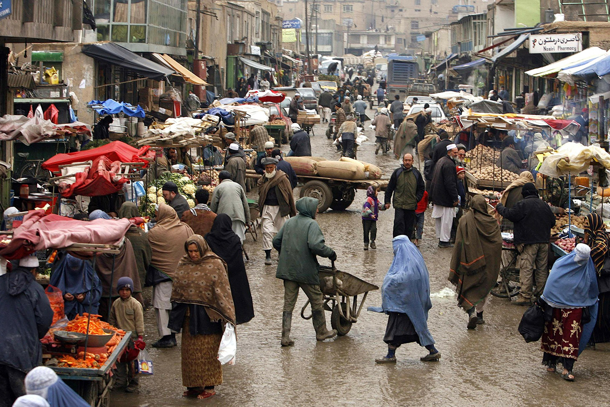 Busy market street in an Afghan town. Men women and children shop at market stalls for fruits and vegetables.