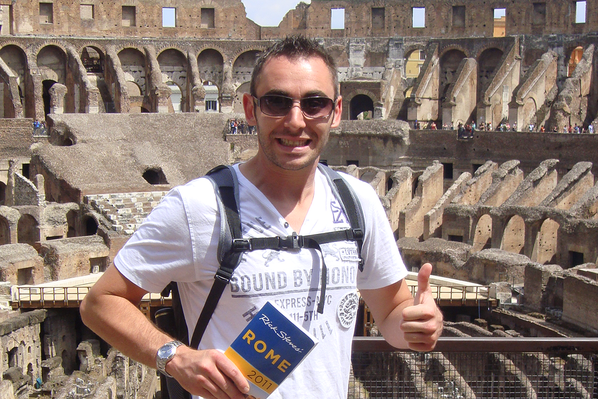 Michael Blakely poses in front of the Coliseum in Rome, Italy, holding a map booklet