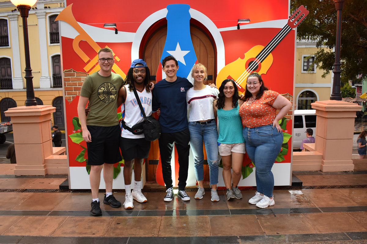 A group of college students pose in front of a musical themed backdrop at a festival in Puerto Rico.