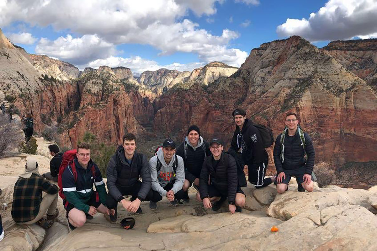 Several college students pose in hiking gear in front of rocky red and tan hills.