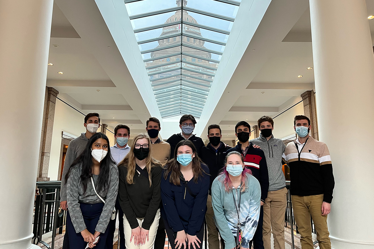 The Entrepreneurship in Austin, TX, class pose as a group in a building, with the Texas capitol building visible through a skylight.