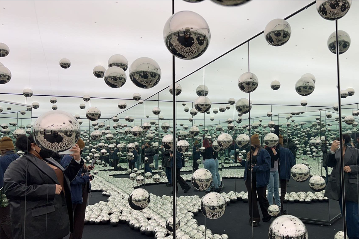 People are scattered throughout an art installation with mirrors and silver balls hanging everywhere.