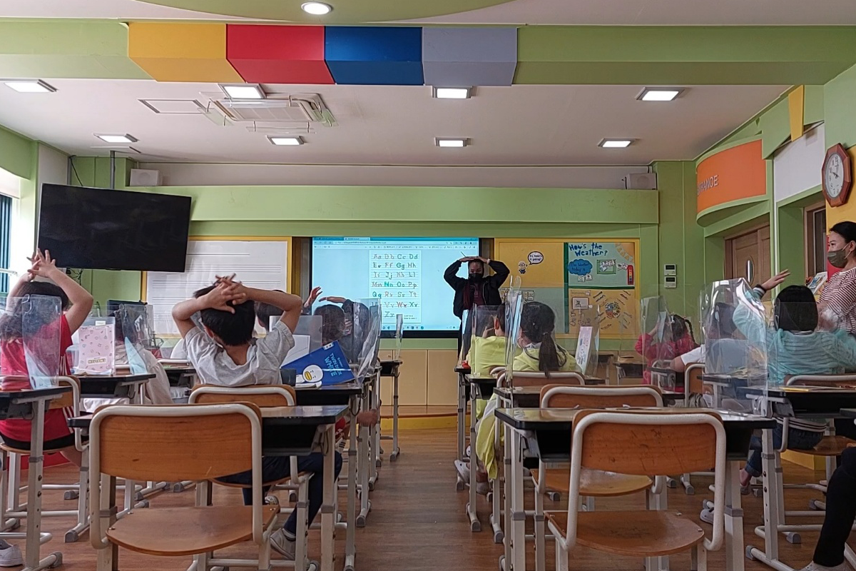 A teacher stands in front of a classroom of children at their desks
