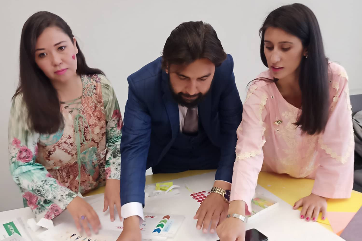 Three Pakistani English teachers work on a presentation board laid out on the table in front of them.