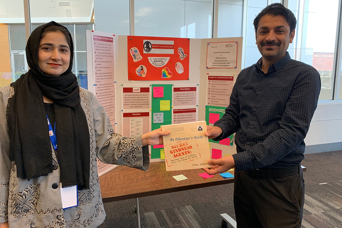 Two teachers stand in front of their trifold display holding a book by Ferial Pearson.