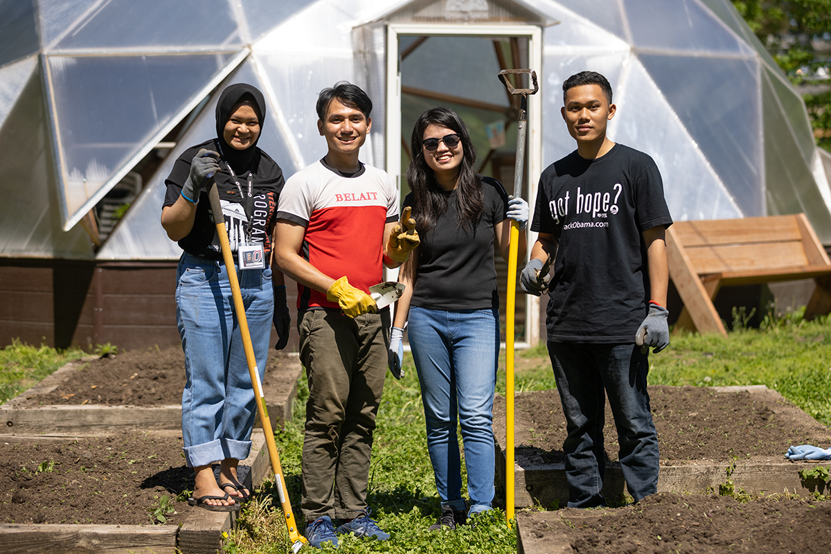 4 YSEALI fellows stand in a garden environment holding gardening tools