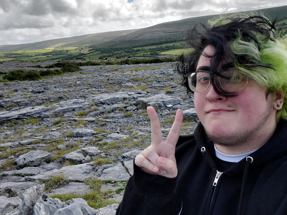 UNO student Kirk flashes a peace sign with his hand in front of the rocky landscape of the Burren.