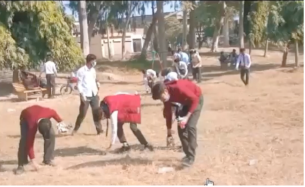 Pakistani teenagers pick up litter in a sandy field.