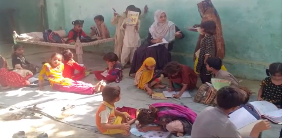 A teacher sits with her students reading on the floor around her in a village school in Pakistan