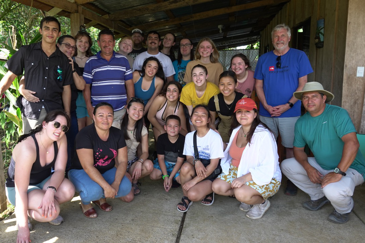 Group of students and staff in Costa Rica pose for a photo under a wooden awning outdoors