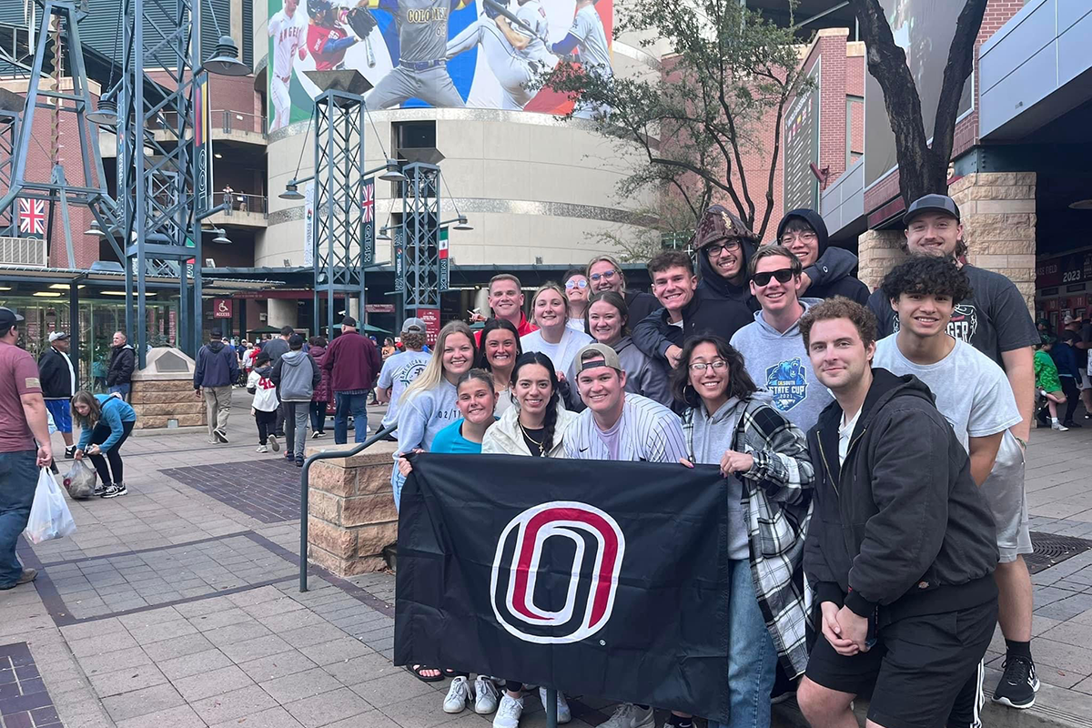 Group of UNO students pose with a UNO flag outside a baseball stadium in Arizona.