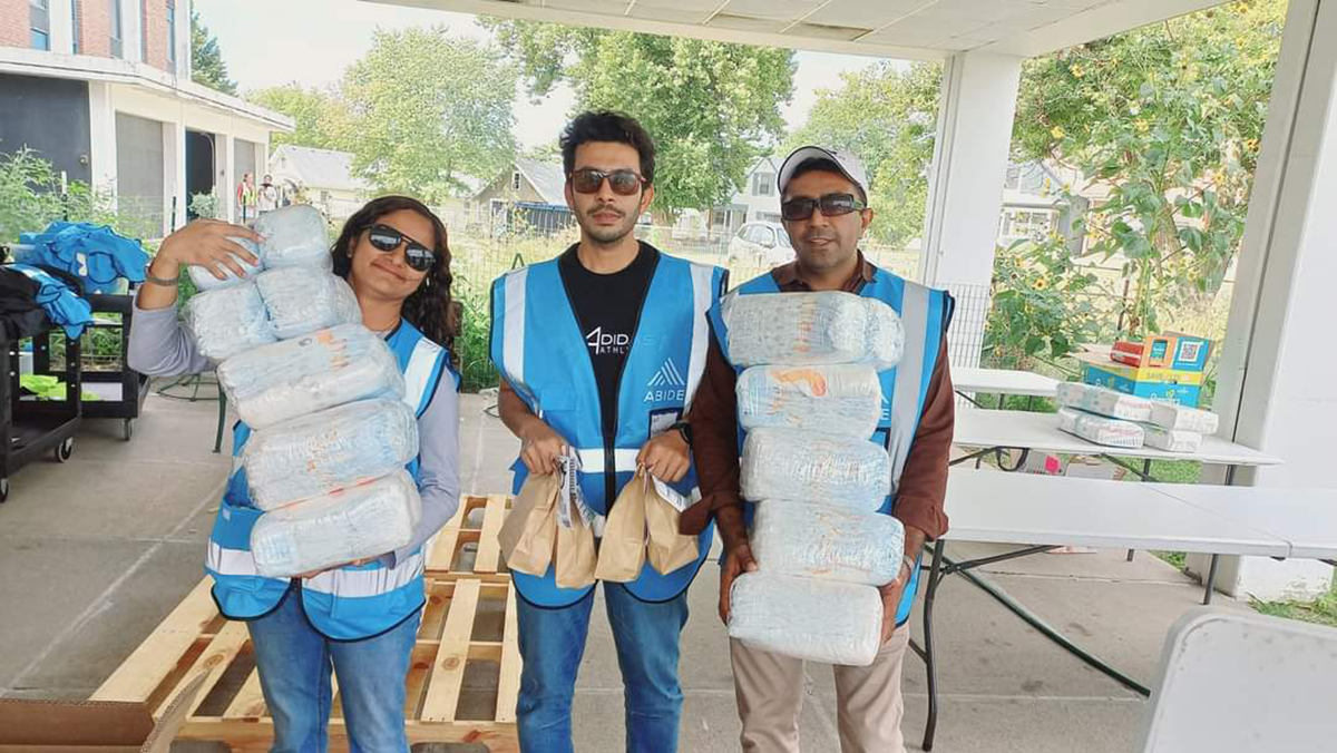 Three people in blue vests hold diaper packs and sack lunches.