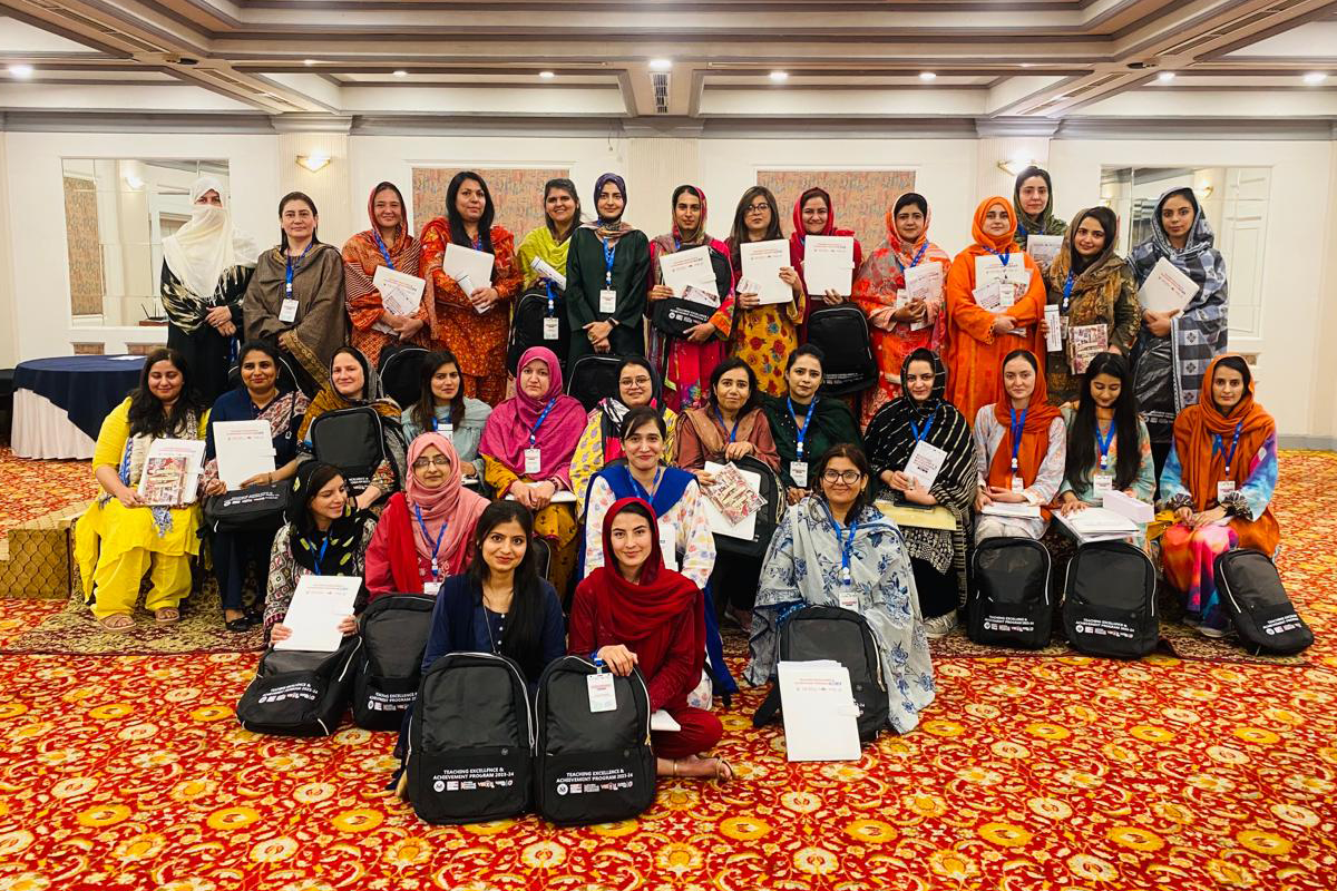 Group of teachers pose together holding handbooks and backpacks.