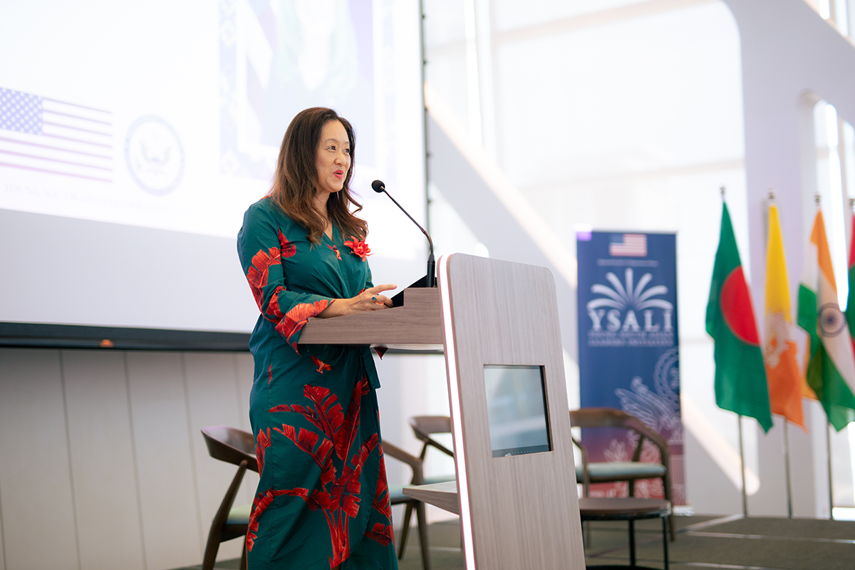 Woman in floral dress speaks at a podium.