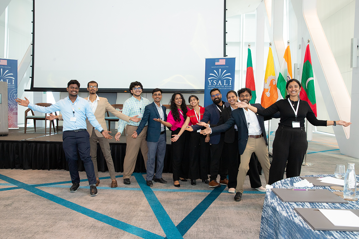 Group smiles and poses in front of a stage and some flags.
