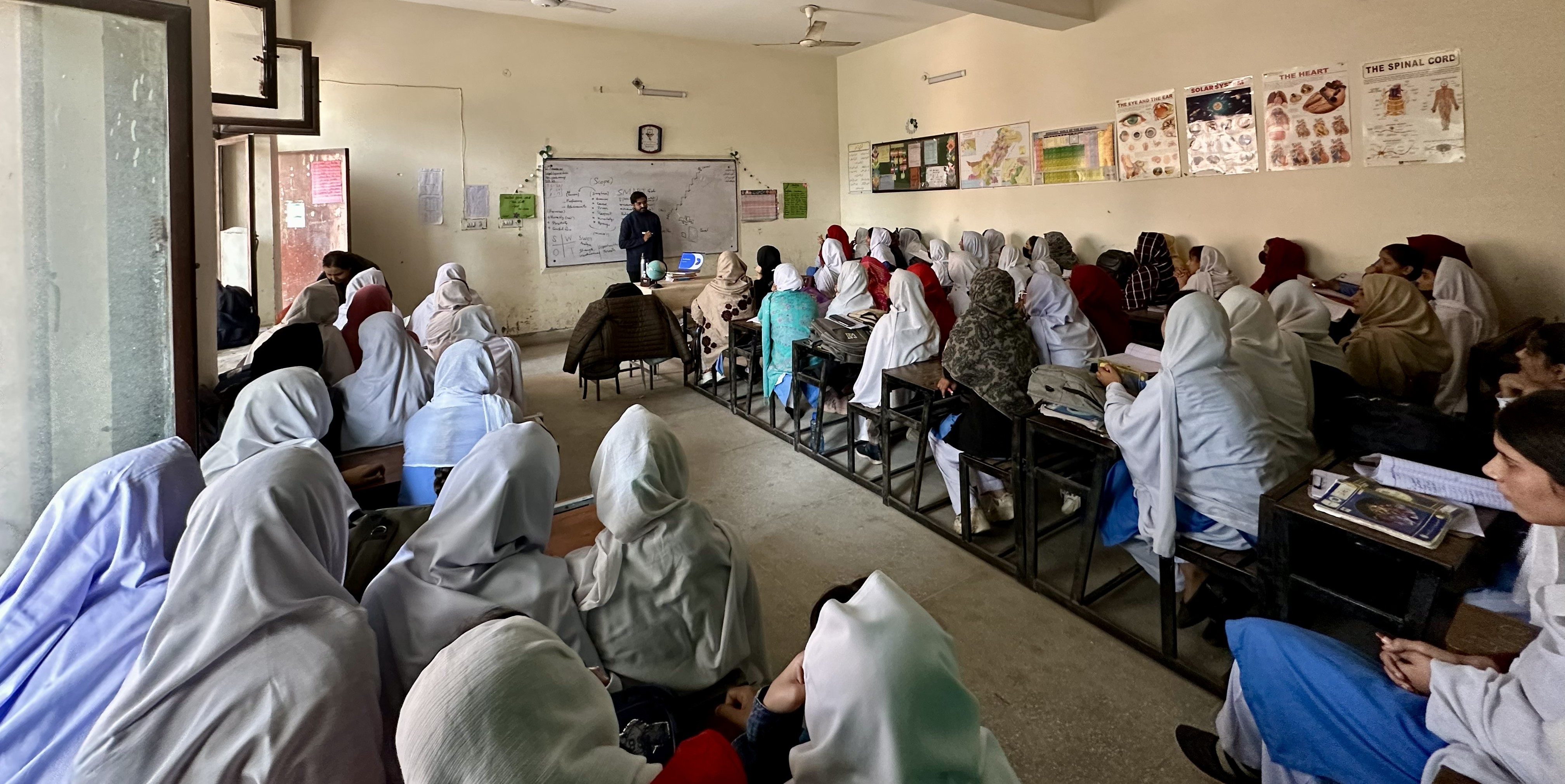 A teacher stands at a whiteboard teaching a room full of women.