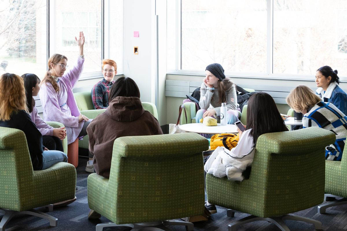 An individual gestures with her arm in the air as a group of students sit and chat.