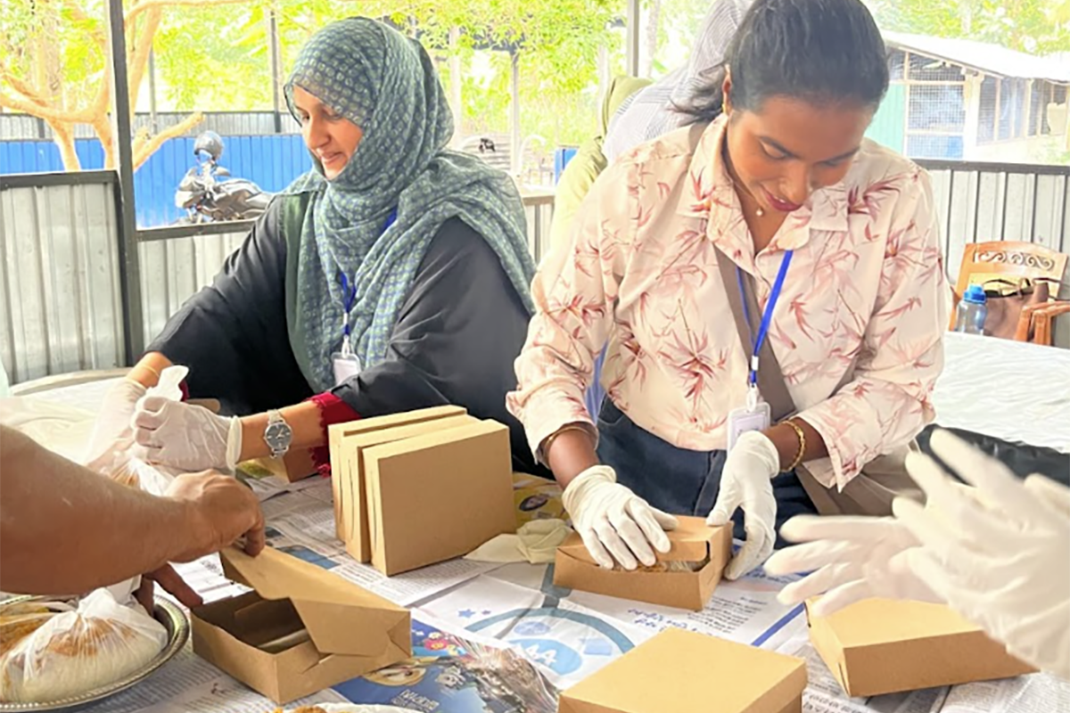 Two women pack food into carryout boxes.