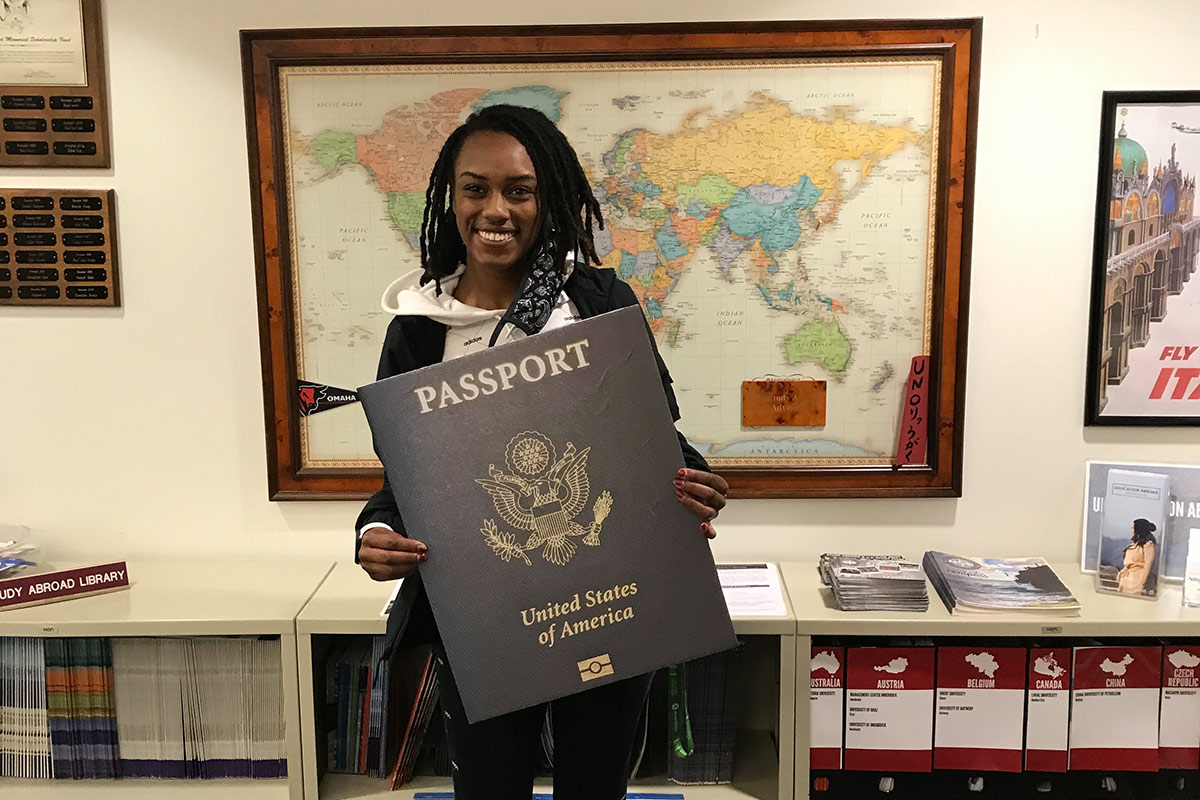 Student holds an oversized cardboard cut-out of a passport.