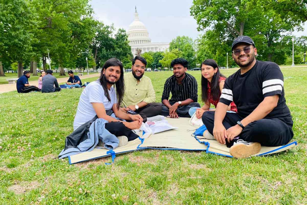 A group of participants sitting together on a blanket in grass networking
