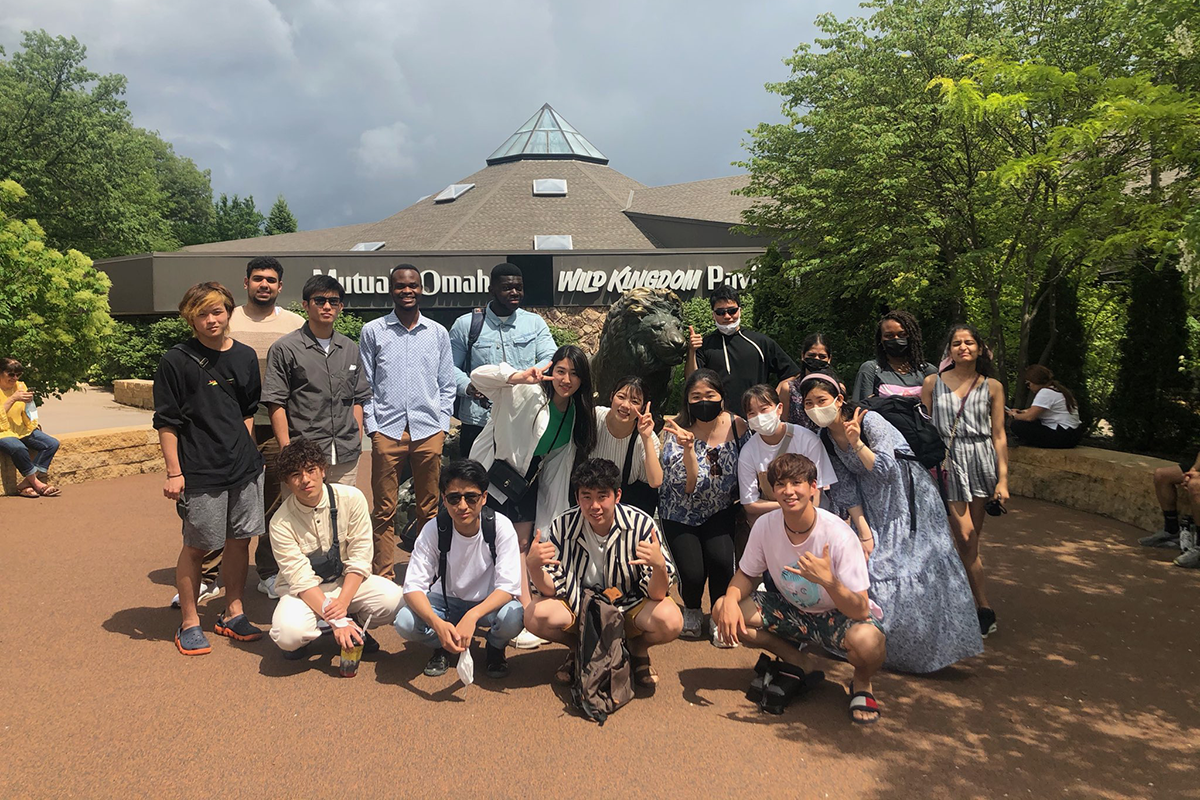 A group of ILUNO students stand around a lion statue at the Omaha Zoo