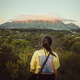 Young woman overlooks treetops and a distant mountain in Stellenbosch, South Africa.