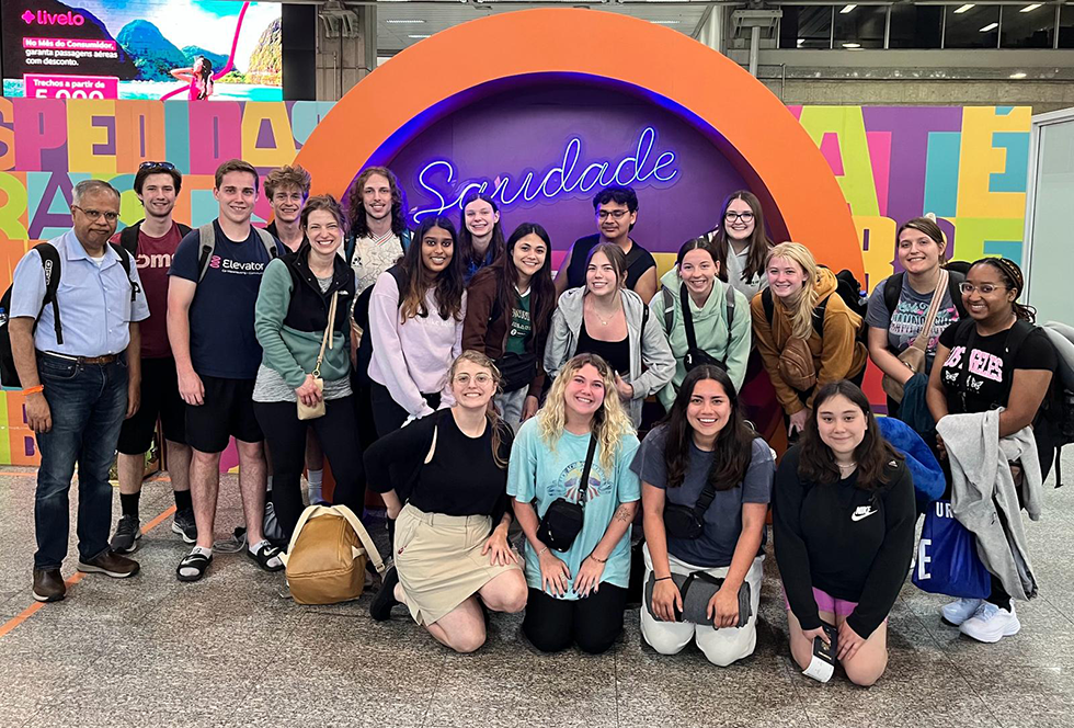 Group of students pose in front of a brightly colored sign in Brazil