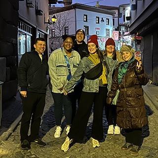 Group poses together, smiling, in a city street at night.