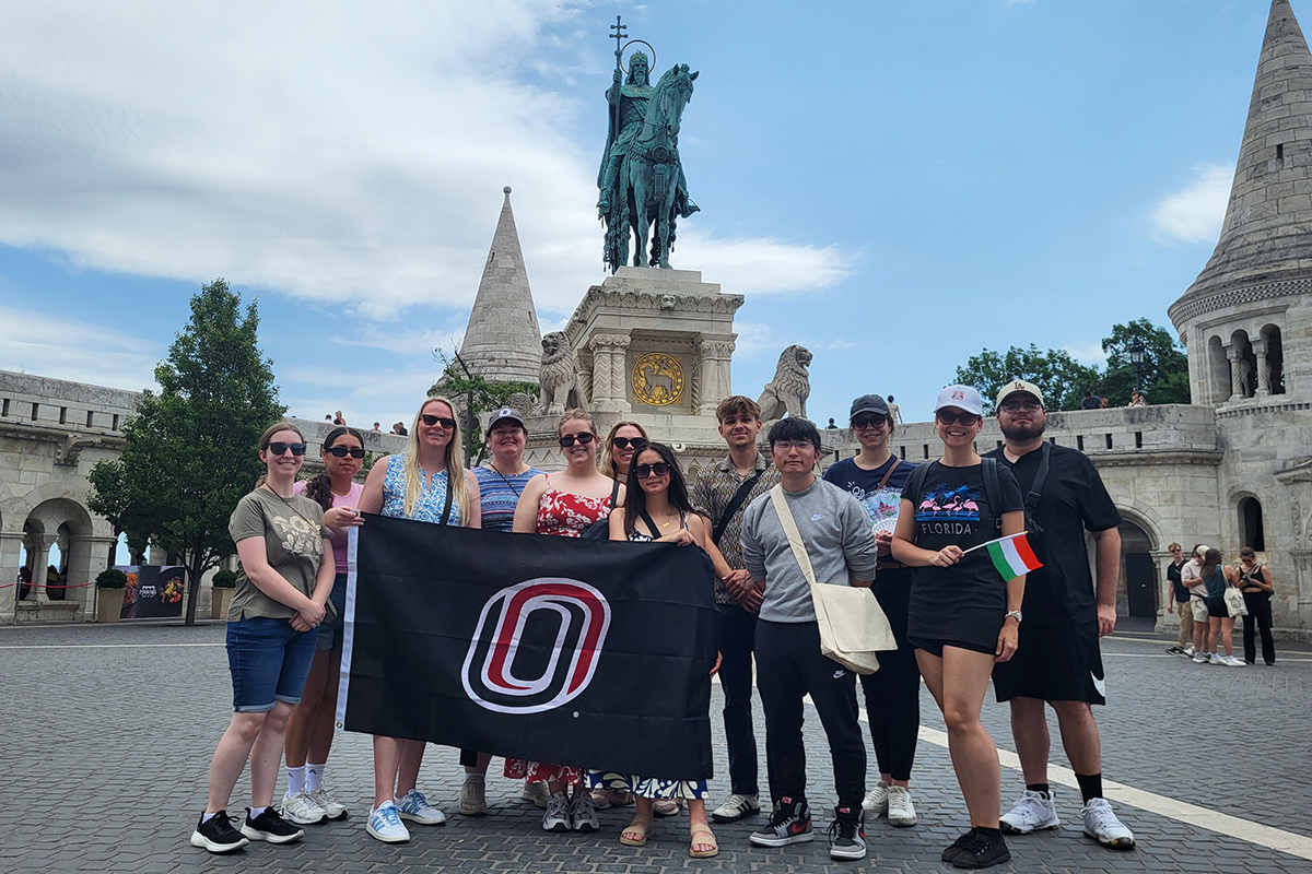 UNO students pose with UNO flag in and outdoor courtyard in Europe