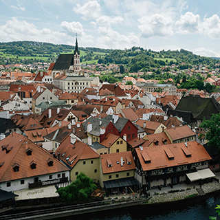 Aerial view of Prague with it's terracotta colored roofs, church spire, and green hills in the distance.