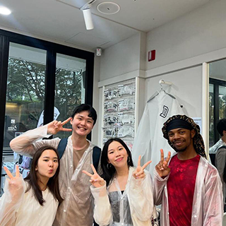 Four college students pose in a shop making peace signs with their hands.