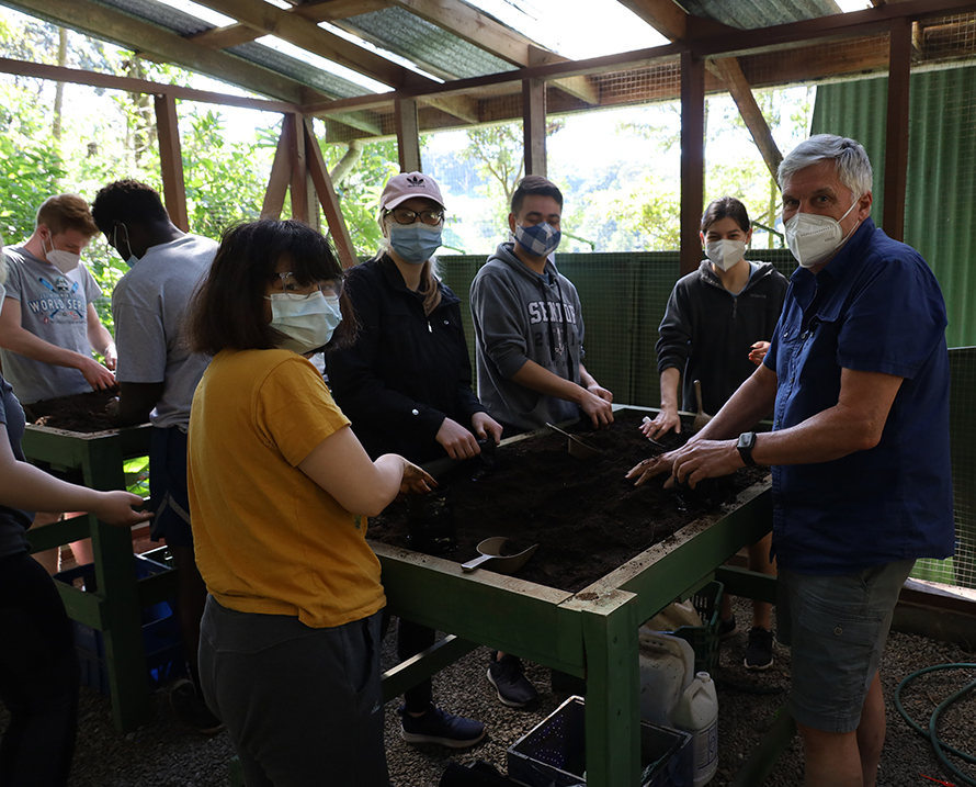 UNO students and their professor gather around a standing planter working on a reforestation project