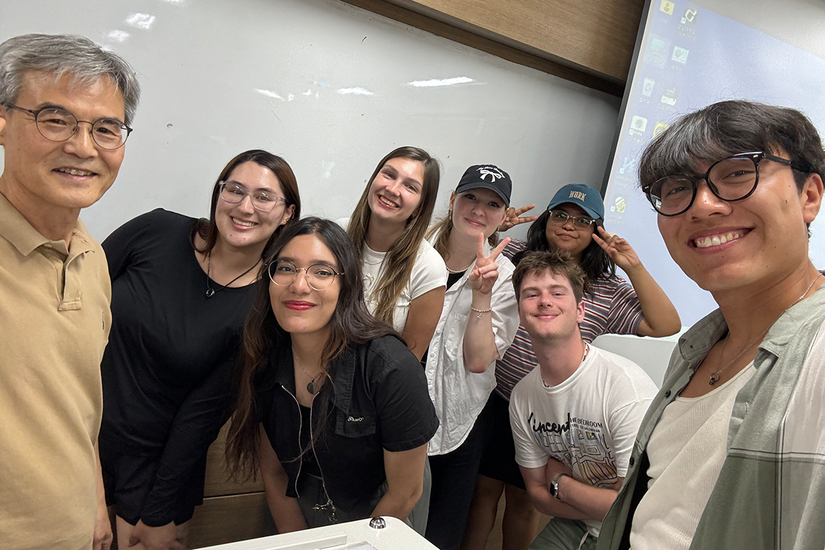 A professor and his students pose together in front of a whiteboard.