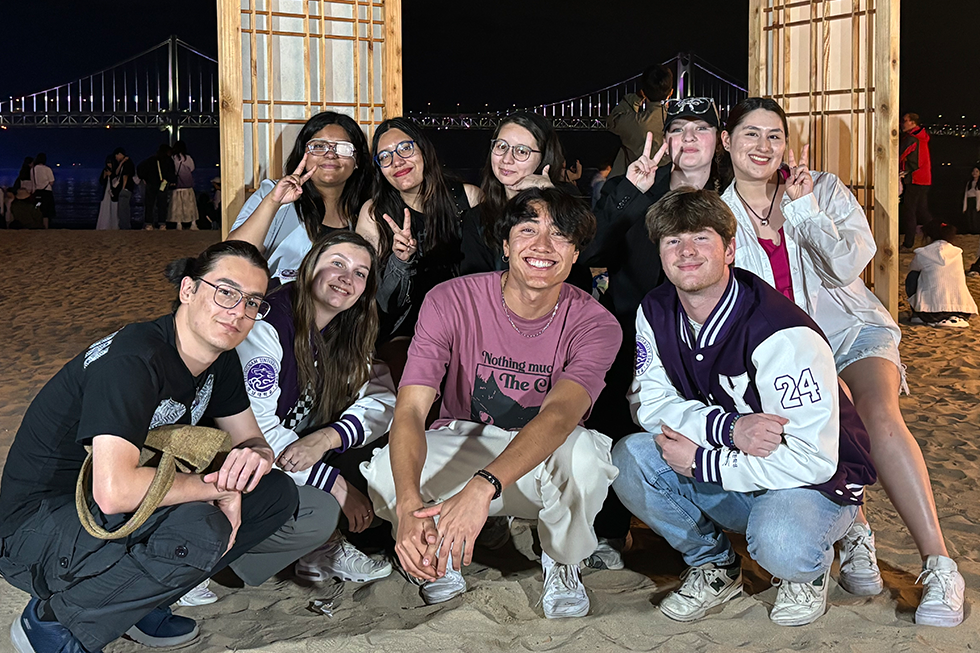 group of students pose together on a beach in Korea at night.