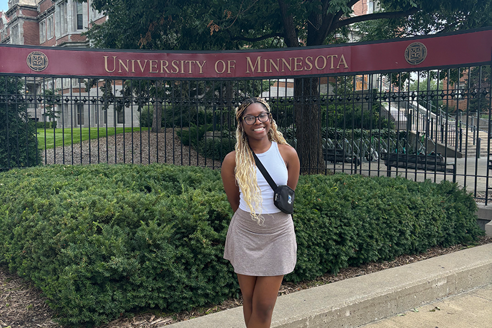 UNO student stands outside in front of the University of Minnesota sign.