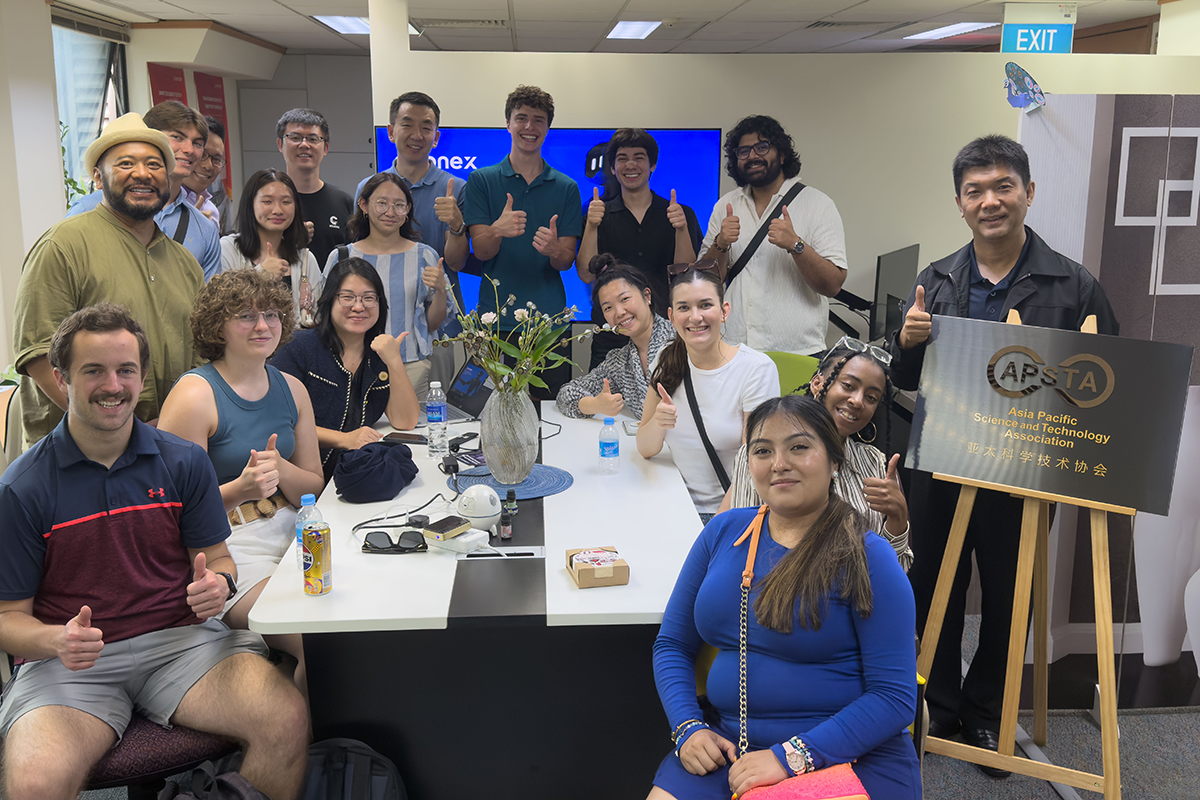 People sitting and standing around a table giving the thumbs up sign.