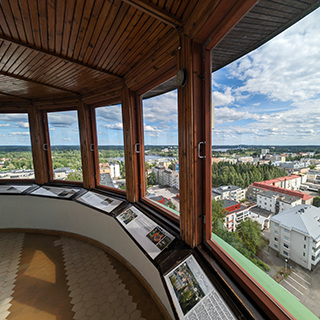 View from inside a building with a wood paneled roof, overlooking a city and trees below.