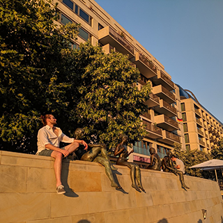 Young man sits on a ledge in line with a row of seated statues.