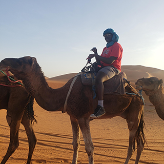 Young man sits on a camel in the sand dunes.