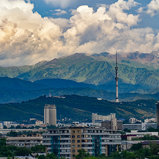 Cityscape in front of a mountain range and blue sky with puffy white clouds.