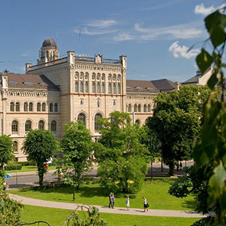 View of a beige stone building with arches, trees, and a walkway at University of Latvia.