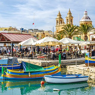 Colorful boats are docked next to a busy riverfront with cafes.