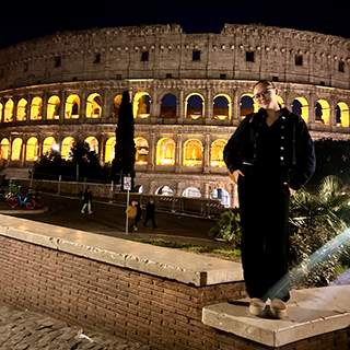 Young woman stands on a ledge in front of the coliseum.